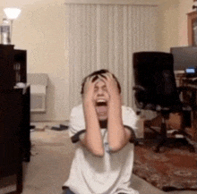 a boy is sitting on the floor with his hands on his head and his mouth open