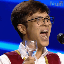 a young man with braces on his teeth is singing into a microphone while holding a glass of water in his hand