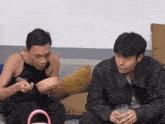 two men are sitting on a couch and one of them is holding a bowl