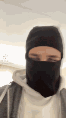 a man wearing a black mask and a white hoodie has tiktok written on his face