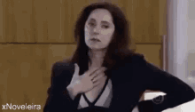 a woman in a suit is holding her hands to her chest and giving a thumbs up .