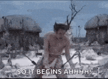 a man without a shirt is standing in a field with a sword in his hand .