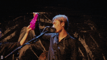 a man in a black shirt is holding a pink and white cloth in front of a microphone