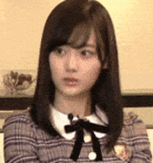 a young woman with long dark hair is wearing a plaid shirt with a black bow and a white collar .