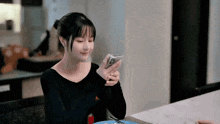 a woman is sitting at a table with a plate of food and looking at her phone .