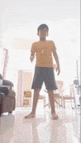 a young boy in a yellow shirt and black shorts is standing on a white floor