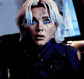 a woman with blonde hair and blue eye makeup is wearing a blue vest and a black jacket .