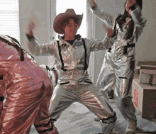 a woman in a cowboy hat is dancing in a room with other people in space suits