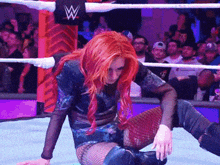 a woman with red hair is kneeling down in a wrestling ring with a w logo in the background