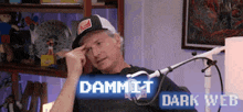 a man in a hat is sitting in front of a microphone with the words dammit dark web above him .