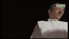 a man wearing a green hat and a white shirt stands in front of a sign for warda productions