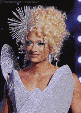 a woman with blonde curly hair is wearing a silver dress and a star shaped headpiece