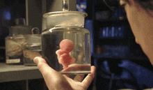 a person is holding a glass jar with a baby in it