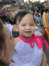 a little girl wearing a white polka dot dress with a pink ribbon around her neck is being held by a woman