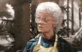 an elderly woman wearing glasses and an apron is sitting in front of a tree .