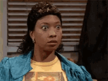 a woman in a blue jacket and yellow shirt is making a surprised face .