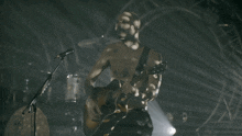 a man without a shirt is playing a guitar in front of a microphone