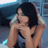 a woman sitting in a chair with her hands on her chin and a bracelet on her wrist