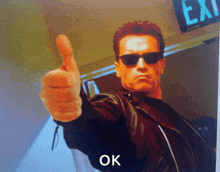 arnold schwarzenegger is giving a thumbs up in front of a exit sign