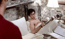 a shirtless man is reading a book while laying in bed