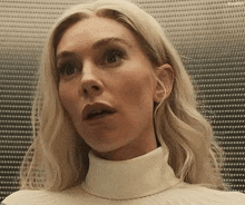 a woman with blonde hair is wearing a white turtleneck sweater and looking surprised .