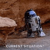 a r2d2 robot is standing in the dirt next to a rock and says `` current situation ? ''