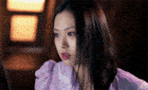 a woman with long black hair is wearing a purple shirt and looking at the camera .