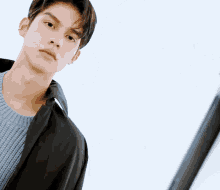 a young man wearing a black jacket and sweater looks at the camera