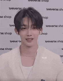 a young man making a heart with his hands in front of a wall that says weverse shop
