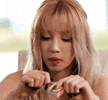 a woman with blonde hair and black nails is holding a matchbox