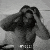 a shirtless man with long hair is holding his hair in a black and white photo and saying hiyeeee .