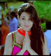 a woman in a pink top and red choker is holding her hands together and smiling .