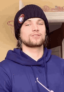 a man wearing a blue hoodie and a black beanie has a patch on his hat that says united states of america