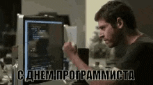 a man is sitting at a desk in front of a computer with russian writing on it .