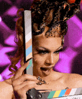 a drag queen is holding a clapper board with a purple background