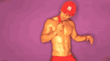 a shirtless man is eating a lollipop while wearing a red ny hat .