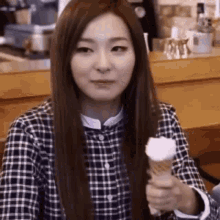 a woman in a plaid shirt is holding an ice cream cone and smiling .