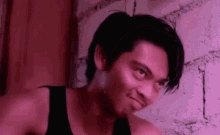 a man in a black tank top is standing in front of a brick wall and making a funny face .