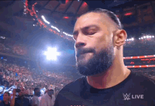 a man with a beard stands in front of a crowd and a sign that says ' w live '