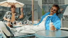 a man in a blue jacket is sitting on a lounge chair holding a milkshake .