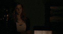 a woman is standing in a dark room with a lamp