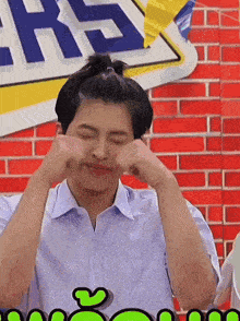 a man in a white shirt is making a face in front of a brick wall
