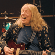 a man with long blonde hair is playing a red guitar