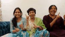 three women are sitting on a blue couch laughing and clapping