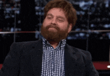 a man with a beard is wearing a plaid shirt and a black jacket
