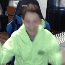 a blurry picture of a man wearing a neon green hoodie and sitting in a blue gtr chair