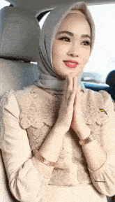 a woman wearing a hijab is sitting in a car with her hands folded in prayer .