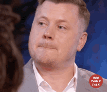a man in a suit and white shirt is looking at a woman with a red table talk logo in the background