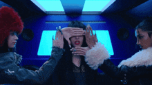 three women covering a woman 's eyes with their hands in a blue room