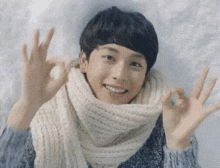 a young man wearing a scarf and a sweater is giving the ok sign .